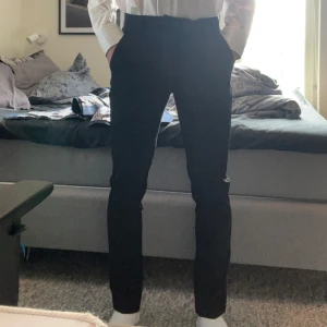 Svarta kostymbyxor från Jack & Jones - Säljer ett par svarta kostymbyxor från Jack & Jones Pants Studio. Byxorna har slim passform, dragkedja och knäppning i midjan. Perfekta till skjorta eller stickad tröja. Klassisk look med smal siluett.som nu ser är den för liten för mig och jag är 180 och väger runt 65 kg. Storlek 28/32