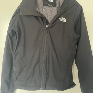 Svart vindjacka från The North Face - Säljer en svart vindjacka från The North Face med dragkedja framtill och huva. Jackan har två sidofickor med dragkedja och meshfoder på insidan. Perfekt för blåsiga dagar och enkel att bära med sig. Använd cirka 2-4 ggr. För fler frågor är de bara att höra av sig🤗