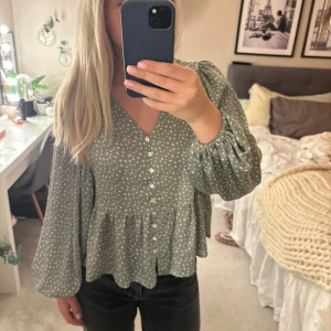 Grön blus med vita prickar och volang - Säljer en söt grön blus med vita prickar och volang nertill. Blusen har långa ärmar med resår vid ärmslut och knappar framtill. Jättefin och bra skick! Storlek s