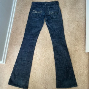 Vintage bebe jeans lowwaist bootcut  - Super lågmidjade bootcut jeans från 2000s bebe. Mörkblå med glitter detaljer på bakfickorna. De är i storlek 25 men skulle säga att de är lite stora i storleken. Midjemått-36cm, innerbenslängd-85cm. Skriv för fler bilder eller frågor!🩷