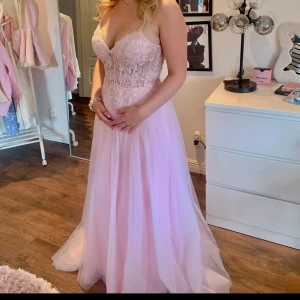 Ljusrosa balklänning - Prinsess ljusrosa långklänning med spetsdetaljer upptill och v-ringad urringning. Klänningen har smala axelband, markerad midja och ett flytande kjolparti i tunt material. Perfekt för bal eller fest. Köpt för 6000kr säljer för 3500