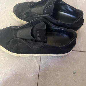 Svarta sneakers från Axel Arigato - Svarta sneakers från Axel Arigato i mocka med vit platt sula. Skorna har en minimalistisk design utan synlig snörning och en rund tå. Perfekta för dig som gillar stilrena och bekväma skor.fråga om ni undrar något🎉🎉