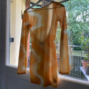 Gul långärmad klänning med djup rygg  - Långärmad kortklänning i mesh med mönster i gul och vit. Klänningen har en djup urringning i ryggen och figurnära passform. NA-KD x Angelica Blick. Storlek XXS, passar även XS. Jättefin till sommarens fester! Använd en gång🌼
