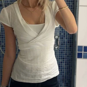 Vit omlottopp - Säljer en jättefin vit omlottopp med guld ränder. Den har korta ärmar och ett knyt där back. Toppen är V-ringad och passar till allt! Den går att använda året runt och är lätt att klä upp och ner. För fler bilder eller frågor är det bara att skriva💖