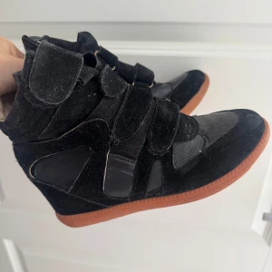 Svarta sneakers med kardborre och brun sula - Säljer ett par svarta sneakers med cool design och flera breda kardborreband. Skorna har en blandning av mocka och syntetmaterial samt en kontrasterande brun gummisula. Perfekta för dig som gillar sportig och trendig stil.