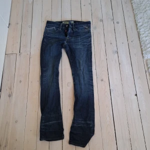 Replay Waitom jeans i mörkblå denim - Säljer ett par Replay Waitom jeans i mörkblå tvätt med klassisk femficksdesign och raka ben. Jeansen har knappar i gylfen och tydliga Replay-detaljer på bakfickan och läderpatch i midjan. Perfekta för dig som gillar en tidlös jeansstil.