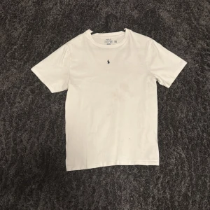 Vit t-shirt från Polo Ralph Lauren - Klassisk vit t-shirt från Polo Ralph Lauren med liten broderad logga i marinblått på bröstet. T-shirten har rund halsringning och är tillverkad i mjuk bomull. Perfekt basplagg med normal passform.