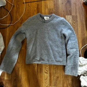 Grå stickad tröja från H&M Edition - Mysig grå stickad tröja från H&M Edition. Tröjan har rund halsringning och långa ärmar, perfekt för kyligare dagar. Enkel och stilren design som passar till det mesta. Materialet känns mjukt och fluffigt. Knappt använd den så verkligen i bra skick!🥰