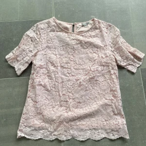 Ljusrosa spetsblus med kort ärm - Söt ljusrosa blus i spets med korta ärmar och rund halsringning. Blusen har ett romantiskt mönster och är perfekt för dig som gillar feminina detaljer.