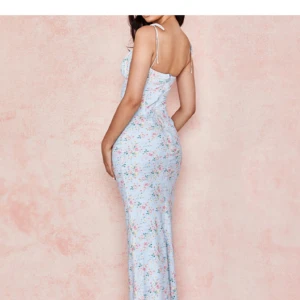 Ljusblå blommig långklänning med smala axelband - Säljer en romantisk ljusblå långklänning med blommigt mönster och smala axelband som knyts upptill. Klänningen har en figurnära passform och söt detalj med liten rosett framtill. Perfekt för sommarens alla tillfällen!