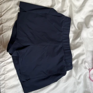Mörkblå träningsshorts från SOC - Mörkblå träningsshorts från SOC med elastisk midja och liten slits i sidan. Perfekta för sport eller gym. Klassisk design utan mönster och i ett lätt syntetmaterial som andas.