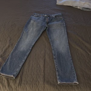 Levis 501 blå jeans - Klassiska blå Levis 501 jeans med raka ben och normal passform. Jeansen har fem fickor, knappgylf och Levis ikoniska läderpatch bak i midjan. Perfekta för en avslappnad stil.