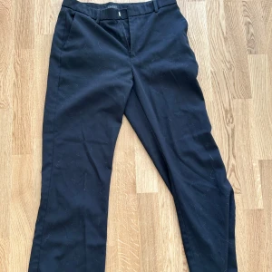 Svarta kostymbyxor med raka ben - Snygga svarta kostymbyxor med klassisk passform och raka ben. Byxorna har hällor för bälte och stängs med dragkedja och knapp. Perfekta till en stilren look.