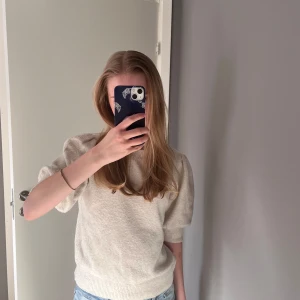 Beige stickad tröja med puffärm - Säljer en beige stickad tröja med korta puffärmar och ribbade muddar. Tröjan har en rund halsringning och är perfekt för lager-på-lager. Enkel och stilren design som passar till mycket.