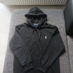 Svart hoodie från Polo Ralph Lauren - Säljer en klassisk svart hoodie från Polo Ralph Lauren med vit broderad logga på bröstet. Perfekt för en stilren look. Nästan helt ny använd fåtal gånger! Kommer nytvättad såklart!