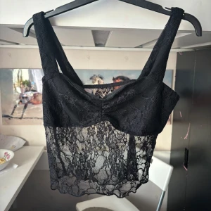 Svart spetsig croppad linnetopp - Säljer en svart croppad linnetopp i spets med breda axelband. Toppen har ett transparent spetsmönster och en lätt v-ringad form framtill. Skriv för fler bilder 💓💓