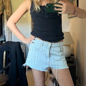 Ljusblå randiga jeansshorts från Zara - Säljer ett par ljusblå jeansshorts från Zara med vita ränder och råa, fransiga kanter. Shortsen har klassisk femficksdesign, bälteshällor och knappgylf. Perfekta för varma dagar och en avslappnad stil.