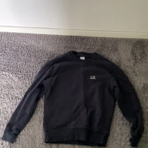 Svart crewneck från C.P. Company - Svart crewneck från C.P. Company med rund halsringning och diskret logga på bröstet. Klassisk modell med långa ärmar. Storlek S men sitter som XS