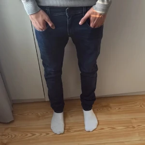 Replay Anbass jeans - Säljer ett par mörkblå Replay Anbass jeans med klassisk femficksdesign och snygga kontrastsömmar. Jeansen har normal passform och raka ben, perfekt för en stilren vardagslook. Märkeslapp bak i midjan och dragkedjegylf.