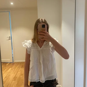 Vit blus med spetsdetaljer från Gina young - Säljer en söt vit blus från Gina young med spetsdetaljer och volang vid axlarna och bröst. Blusen har v-ringning och är kort i ärmarna. Ser skrynklig ut på bilden men går att stryka. Varan är använd fåtal gånger och därför finns inga defekter. Storlek 158/164🩷