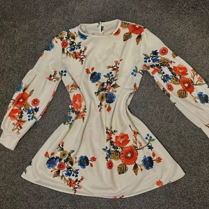 Vit blommig klänning med långa ärmar👗💐 - Superfin vit klänning med färgglada blommor i rött, blått och orange. Klänningen har långa ärmar med lätt puff och en rund halsringning. Perfekt för vår eller sommar och ger en fräsch och glad look🤭🦋