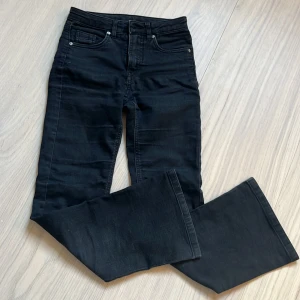 Svarta jeansbyxor från Kappahl - Svarta jeansbyxor från Kappahl med klassisk femficksdesign och bootcut ben. Byxorna har knapp och dragkedja i midjan samt bälteshällor. Perfekta för en stilren och enkel look.