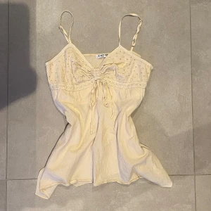 Beige linnetopp från S'WEST - Säljer en söt beige linnetopp från S'WEST med tunna axelband och broderade prickar upptill. Toppen har knytning framtill och är lätt utsvängd nertill. Perfekt för varma dagar och enkel att styla. En liten fläck på baksidan men inget man tänker på så mycket😊