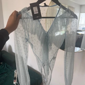Ljusblå mesh topp från Fashion Nova - Superfin ljusblå mesh topp från Fashion Nova med prickigt mönster och volangdetaljer längs v-ringningen. Toppen är långärmad och har transparent material som ger en cool och trendig look. Perfekt att styla lager på lager.