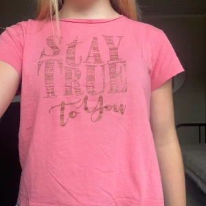 Rosa t-shirt med tryck från KappAhl - Rosa t-shirt från KappAhl med texten 'Stay True to You' i ett coolt mönstrat tryck på bröstet. Klassisk rund halsringning och korta ärmar. Skön och mjuk i bomull, perfekt för en chill och avslappnad stil.