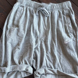 Grå mjuka shorts från Nike - Gråa mjukisshorts från Nike med elastisk midja och snörning. Klassisk logga på ena benet och två sidofickor. Perfekta för chill eller träning, tillverkade i mjuk bomullsmix som känns skön mot huden.