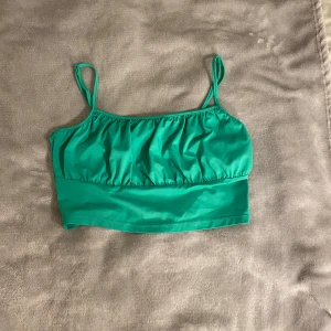 Grön linnetopp - Snygg grön linnetopp med smala axelband och rynkad överdel. Toppen är croppad och har en enkel, stilren look som passar perfekt till jeans eller kjol. Tillverkad i ett mjukt, stretchigt syntetmaterial som känns skönt mot huden. Använd 1 gång