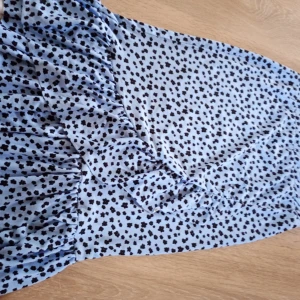 Blommig blå volangkjol - Supersöt blå kjol med svarta blommor och volangkant nertill. 💕Kjolen har en rak passform och resår i midjan för extra komfort. Materialet känns mjukt och Kjolen är nästan alldrig andvänd.💕(Finns katt i hemmet)💕