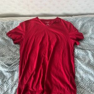 Röd v-ringad t-shirt från Goodfellow - Röd t-shirt från Goodfellow & Co i modellen Lyndale Tee. T-shirten har v-ringning, korta ärmar och är gjord i mjuk bomull. Enkel och clean design som passar perfekt till jeans eller shorts.