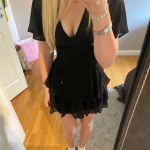 Svart volangklänning med inbyggda shorts - Supersöt svart kortklänning med v-ringning och volangdetaljer. Klänningen har inbyggda shorts. Ändast testad, lappen sitter kvar. 🩷