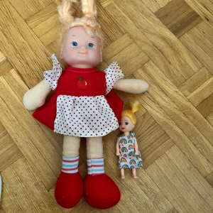 Röd prickig dockklänning med äpple - Supergullig röd dockklänning med vitt förkläde och röda prickar, samt ett broderat äpple på bröstet. Puffiga korta ärmar och rund hals. Klänningen är sydd i bomullstyg och har en klassisk, lekfull stil som passar perfekt till dockor.