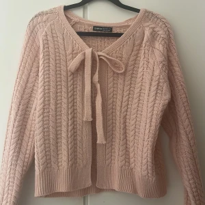 Ljusrosa stickad kofta från SHEIN - Supersöt ljusrosa stickad kofta från SHEIN med kabelstickat mönster och knytband framtill. Koftan har långa ärmar och ribbade muddar vid ärmslut och nederkant. Perfekt för lager-på-lager och ger en gullig vibe till din outfit. Använd 3-4 gånger max.