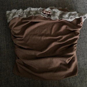 Brun ribbad topp med spets kant - Söt brun ribbad topp med spetskant upptill och en liten rosett i mitten. De är mycket stretch i så passa M och L oxå.
