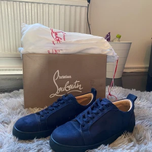 Mörkblå sneakers från Christian Louboutin - Säljer ett par snygga mörkblå sneakers från Christian Louboutin i mocka med klassisk röd sula och broderad logga på hälen. Skorna har rund tå, platt sula och blå snörning. Insidan är i beige skinn och detaljerna är riktigt lyxiga. Box och dustbag medföljer.