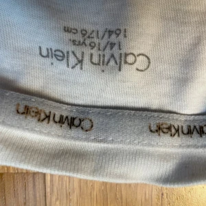 Vit t-shirt från Calvin Klein - Vit t-shirt från Calvin Klein med klassisk rund hals och diskret CK-logga tryckt på bröstet. Tillverkad i mjuk bomull som känns skön mot huden. Enkel och stilren design som passar perfekt till jeans eller shorts. 100kr