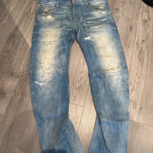 Ljusblå slitna jeans från G-Star - Säljer ett par ljusblå jeans från G-Star med coola slitningar och distressed detaljer både fram och bak. Jeansen har raka ben och klassisk femficksdesign. Perfekta för dig som gillar en avslappnad streetstil.
