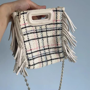 Rutig axelväska med fransar från Maje - Superfin axelväska från Maje i rutigt tyg med inslag av vitt, svart, rosa och blått. Väskan har coola fransar på sidorna, silverfärgad kedja och handtag i ljust skinn. Perfekt för dig som vill sticka ut med en unik accessoar.