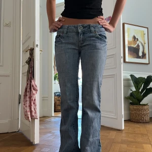 Blå bootcut jeans med fickdetaljer - Säljer ett par blå bootcut jeans med låg midja och snygga fickdetaljer bak. Jeansen har klassisk femficksdesign, ljus tvätt och raka ben som blir lite vidare nertill. Perfekta för dig som gillar en avslappnad men ändå trendig look.