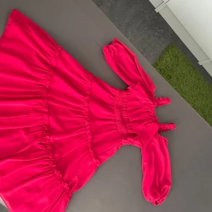 Rosa volangklänning med puffärm - Säljer en superfin rosa kortklänning med volanger och puffiga långärmar. Klänningen har smock i midjan och axelband med volangdetaljer. Perfekt för dig som gillar färgstarka och trendiga plagg med mycket detaljer.