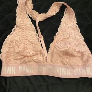 Rosa spets bandeau från PINK - Supersöt bandeau topp från PINK i ljusrosa med bred resår där det står PINK i glitter. Spets framtill och mesh på insidan, med snygg detalj i ryggen. Perfekt för att ge din outfit en extra touch av stil.