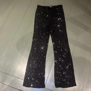 Svarta paljettbyxor från Lindex - Glittriga svarta byxor från Lindex med paljetter över hela ytan. Byxorna har rak passform och elastisk midja för skön känsla. Perfekta för dig som vill sticka ut med lite extra bling och cool vibe. Passar dig som gillar att synas och vill ha något unikt i garderoben☺️