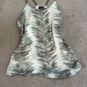 mönstrad linnetopp från Vila - Snygg linnetopp från Vila i storlek S med tunna svarta axelband. Toppen har ett coolt abstrakt mönster i grått, svart och ljusblått på vit bakgrund. Luftig och lätt, perfekt för varma dagar. Passar dig som gillar en chill och trendig stil. Lite slitna straps (sista bilden)