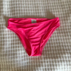 Rosa bikiniunderdel från KappAhl - Snygg och enkel bikiniunderdel från KappAhl i en stark rosa färg. Klassisk modell med mjuka sömmar och stretchigt syntetmaterial som sitter bekvämt. Perfekt för strandhäng och pooldagar i sommar. Passar dig som gillar färgstarka badkläder.