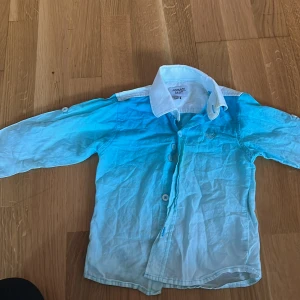 Blåvit skjorta från Armani Baby - Snygg skjorta från Armani Baby i blå och vit ombre med klassisk krage och knappar framtill. Skjortan har lång ärm och broderad logga på bröstet. Perfekt för dig som vill ha något stilrent och trendigt till de små. Kan diskutera om priset:)