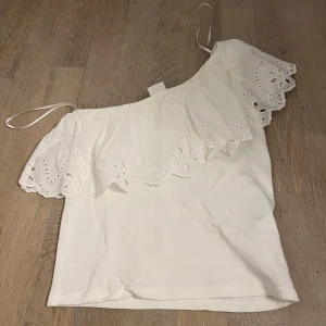 Vit offshoulder topp med volang från Zara - Supersöt vit offshoulder topp från Zara med bred volangkant och broderade blommor. Tunn ribbad botten och axelbandslös design som ger en chill och somrig vibe. 