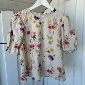 Blommig blus från VILA, strl 34 - Supersöt blommig blus från VILA i storlek 34. Blusen har puffiga korta ärmar med resår och ett färgglatt blommönster i rosa, lila, gul och röd på en ljus bakgrund. Rund halsringning och knapp i nacken. Perfekt för vår och sommar!